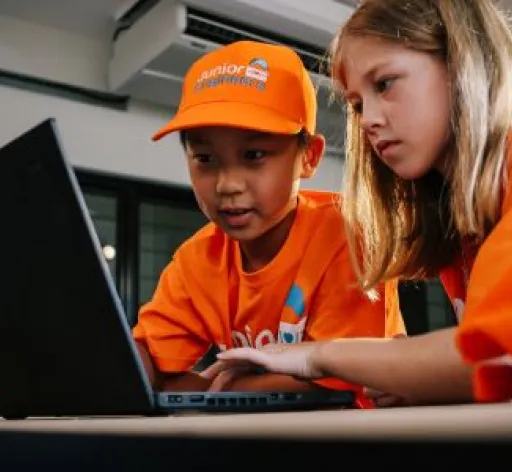two children play at a computer wearing Junior Engineers branded hat and tshirts 