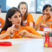 image of tutor and children in conversation wearing orange shirts sitting around white tables 
