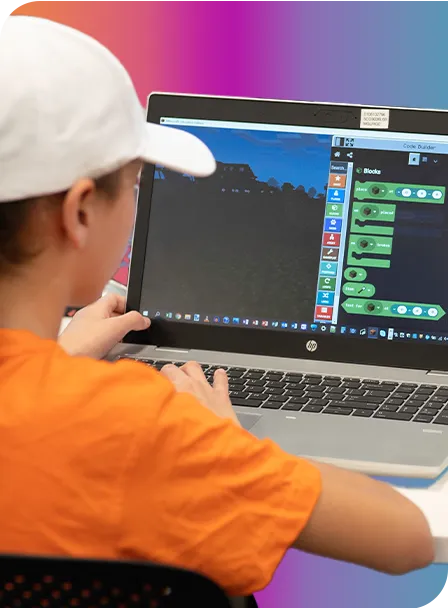 girl sitting at laptop in front of coloured background wearing a white hat and orange shirt